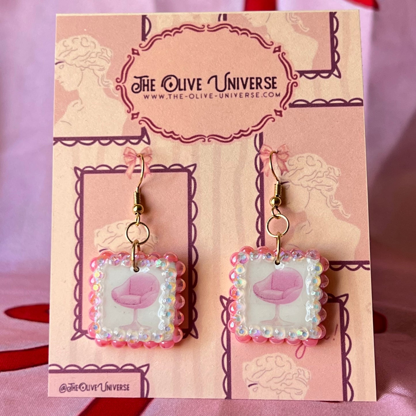 Handmade polymer‑clay earrings featuring a vintage mid‑century pink chair graphic framed by pink pearls and rhinestones on 18k gold‑plated hooks, perfect retro, vintage, indie, Y2K‑style statement dangles.