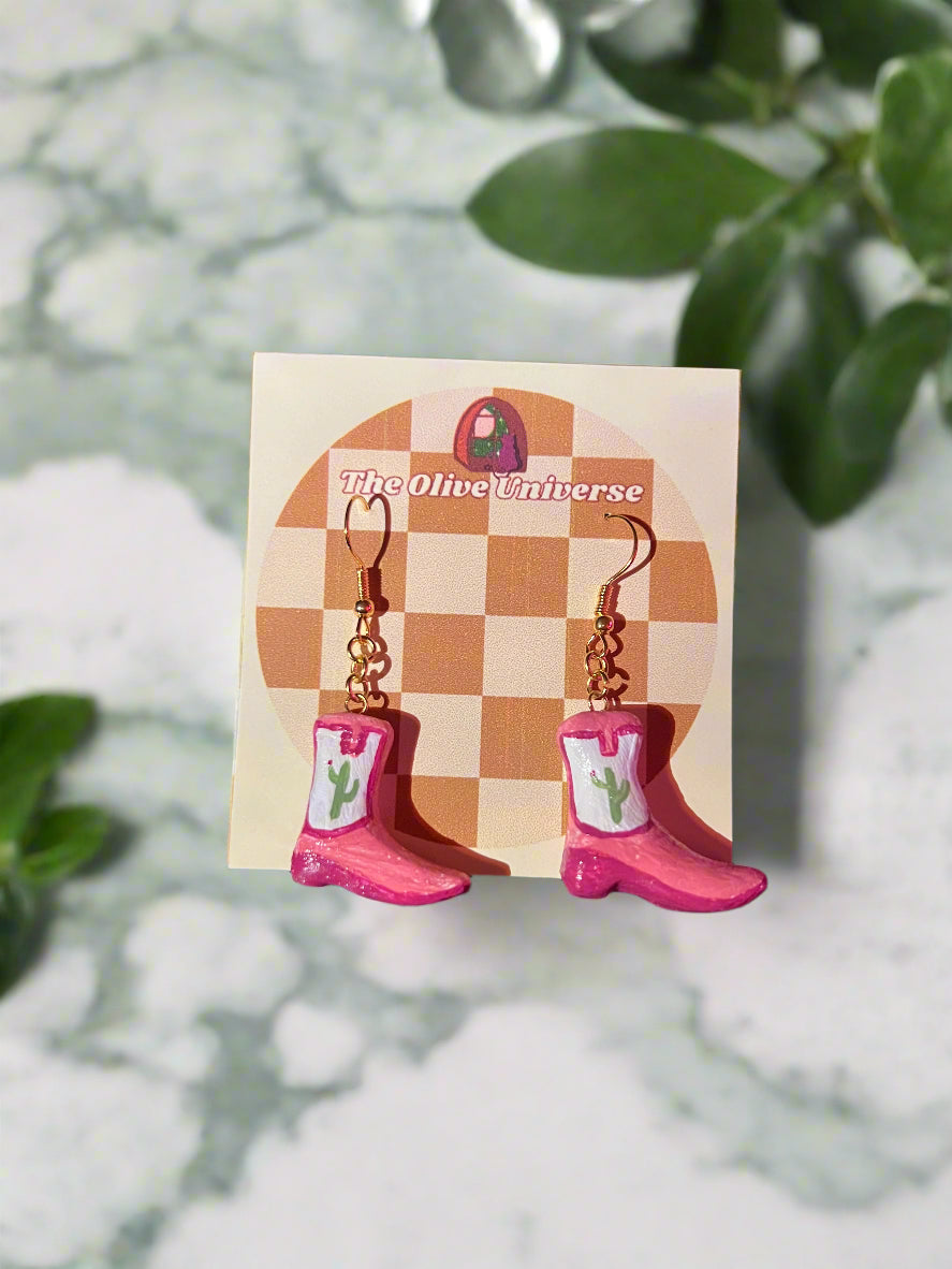 Pink cowboy boot keychains on a checkered card with 'The Oliver Universe' branding.