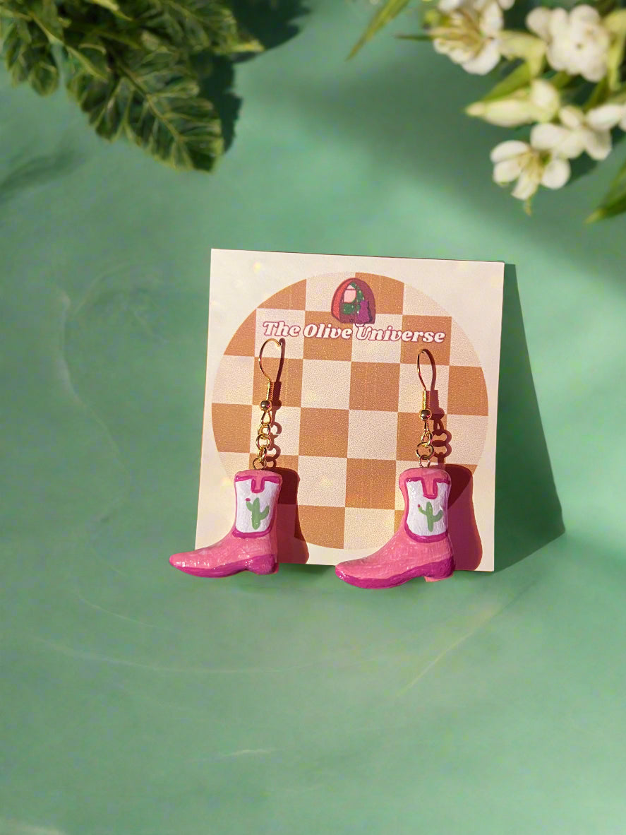 Pair of earrings on a card with a checkered design, surrounded by makeup items on a dark background.