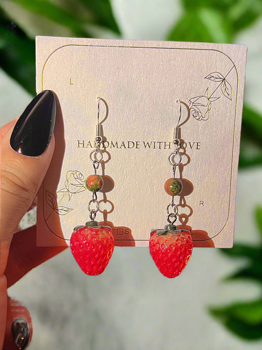 Strawberry-shaped earrings on a 'Handmade with Love' card held by a hand.