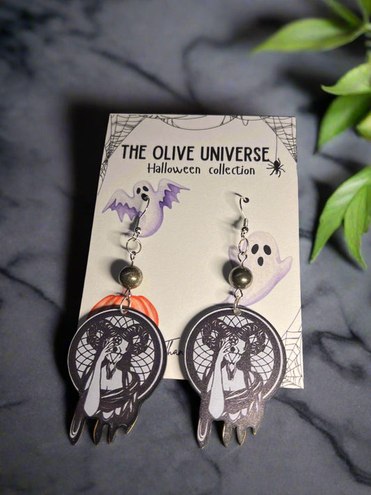 Halloween-themed earrings with dark witchy woman holding a mask. Features occult mask and symbolism. Spooky season earrings on a 'The Olive Universe' branded card with a ghost, pumpkin, and spiderweb background.