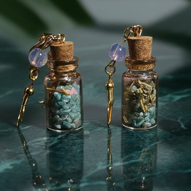 Pair of witchy earrings made of small bottles with cork lids, filled with amazonite stones and opal beads, on a green leaf background. cute halloween earrings spell jar earrrings