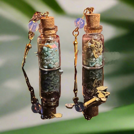 Pair of witchy earrings made of small bottles with cork lids, filled with amazonite stones and opal beads, on a green leaf background. cute halloween earrings spell jar earrrings