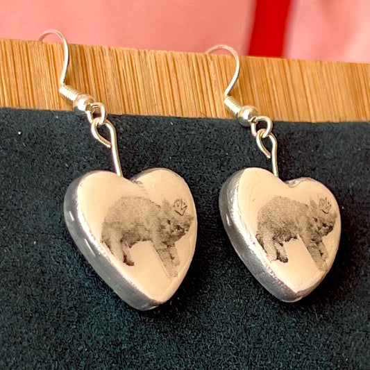 Alt text: Handmade white polymer‑clay heart earrings featuring a black‑and‑white crowned kitten, described as sweet, slightly regal, and perfect for coquette/kawaii styling, with hypoallergenic silver‑plated hooks; ideal cat‑lover gift and cute statement jewelry.
