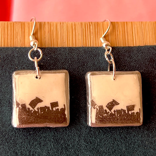 Alt text: Activist “for the people” protest earrings featuring handmade polymer clay silhouette charms with a silver‑black metallic finish, silver‑plated hypoallergenic hooks, and bold protest jewelry style.