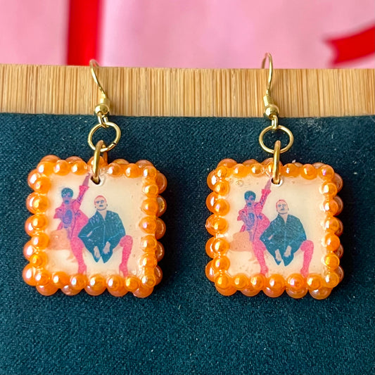 Handmade queer art earrings featuring polymer‑clay square charms with a “Strike a Pose” design, iridescent orange pearl drops, and 18k gold‑plated hypoallergenic findings – lightweight square charms, LGBTQ‑pride, statement piece, ready to ship in 1–3 days.