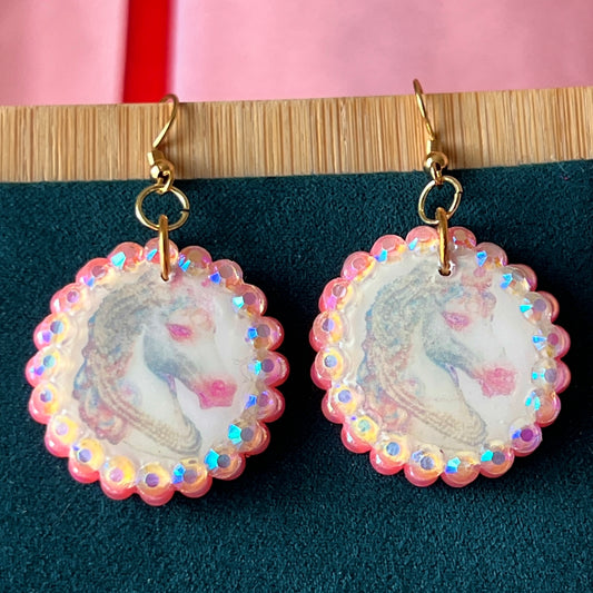 Alt text: "Handmade unicorn earrings featuring a pastel polymer‑clay charm with a soft fairy‑core illustration, bedazzled by iridescent pink pearls and white gems, set in a gold‑plated fishhook finding; a whimsical, sparkly dangle earring perfect for Y2K, coquette, and pastel jewelry styles."