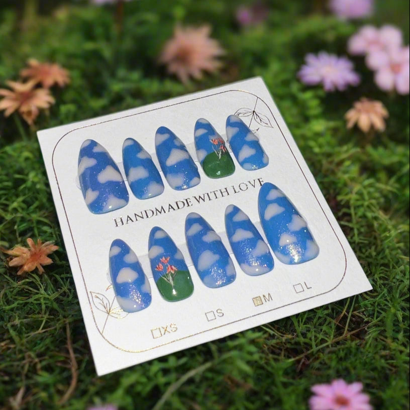 Nail art stickers with blue skies and fluffy white clouds and green meadow with flower design on a grassy background