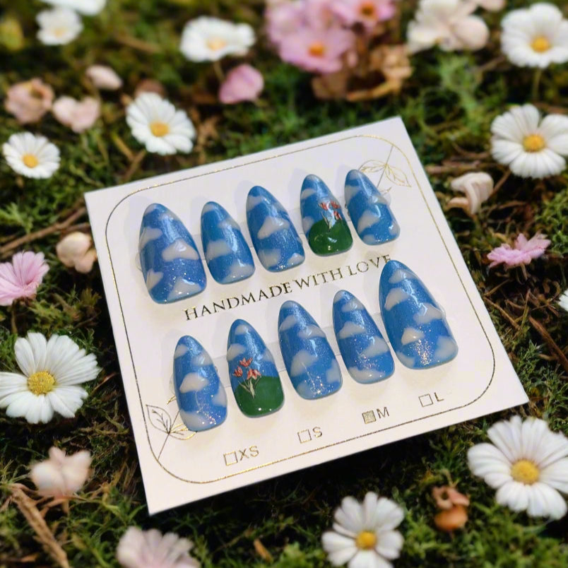 Nail art display with blue and white designs on a card, surrounded by flowers.