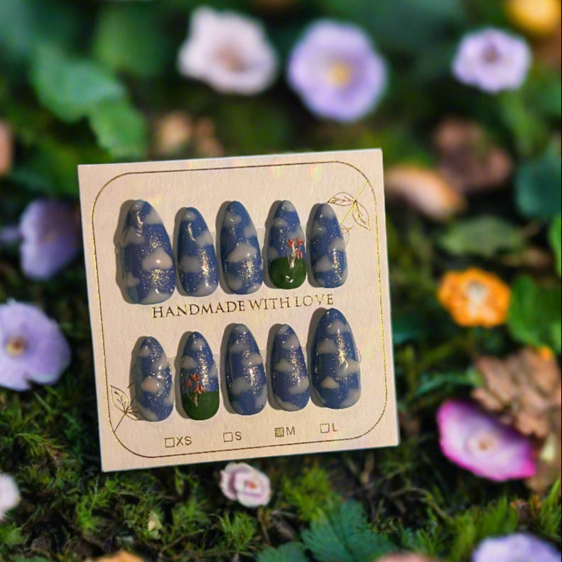 Set of blue and green nail art designs on a cardboard backing with 'Handmade with Love' text, placed on a natural background with flowers.