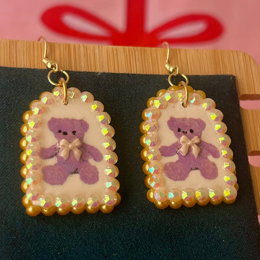 Handmade golden teddy bear bow charm earrings made from polymer clay with image transfer, featuring a 0.5‑inch arch charm framed by golden pearls and rhinestones, 18k gold‑plated hypoallergenic findings, luxuriously weighted, perfect teddycore, coquette, toycore, Y2K style statement piece.