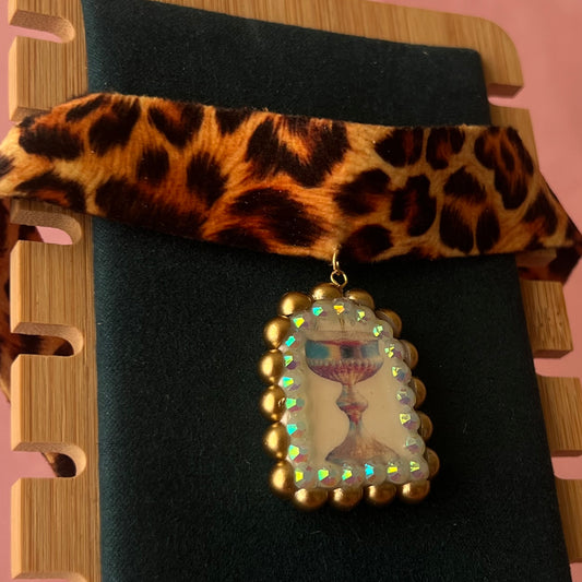 Jungle Elixir choker — soft cheetah print choker with handmade polymer clay fantasy chalice charm framed with bronze pearls and iridescent rhinestones. Adjustable fit ~14–16" with extension chain. Gift-ready green Victorian-patterned box + bow. Ready to ship in 1–3 days.