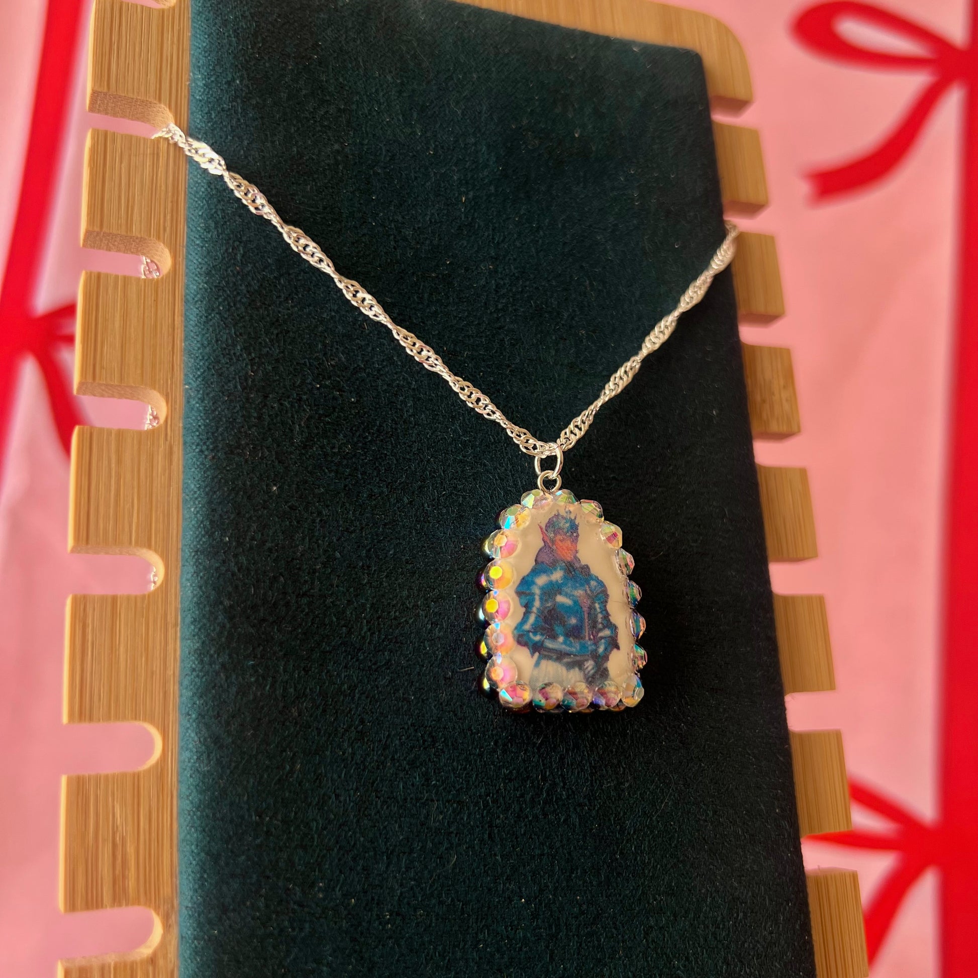 Elf Knight Necklace by Olive Made — a handmade polymer clay fantasy charm necklace featuring a medieval-inspired elf in knight armor, embellished with iridescent pearls and sparkling rhinestones. This whimsical medievalcore / fairycore statement piece comes on a 20” 925 sterling silver chain and arrives gift-ready in a Victorian patterned box with a green bow. Perfect for renaissance fair outfits, elfcore styling, and storybook gifting. Ready to ship in 1–3 business days.