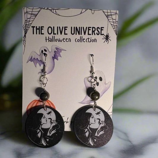 Halloween-themed witch with snake spooky season earrings on a branded card with ghost, spider web, and pumpkin illustrations. Includes hematite beads and vintage y2k witchy vibes