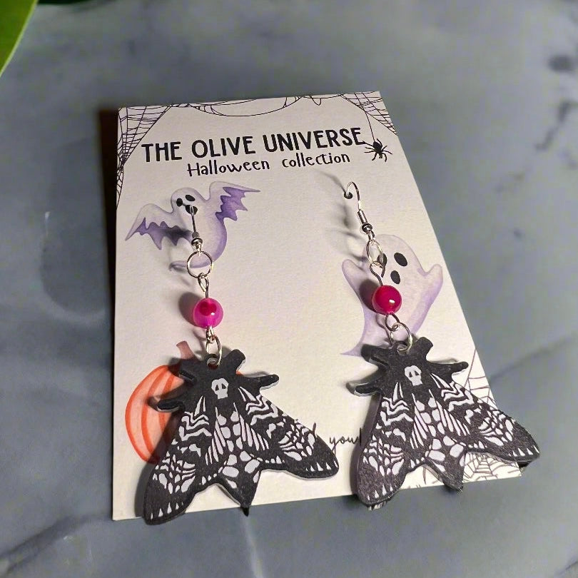 Halloween-themed moth earrings with gothic pattern and pink agate. crystal gemstone bead on a card with 'The Olive Universe' branding.