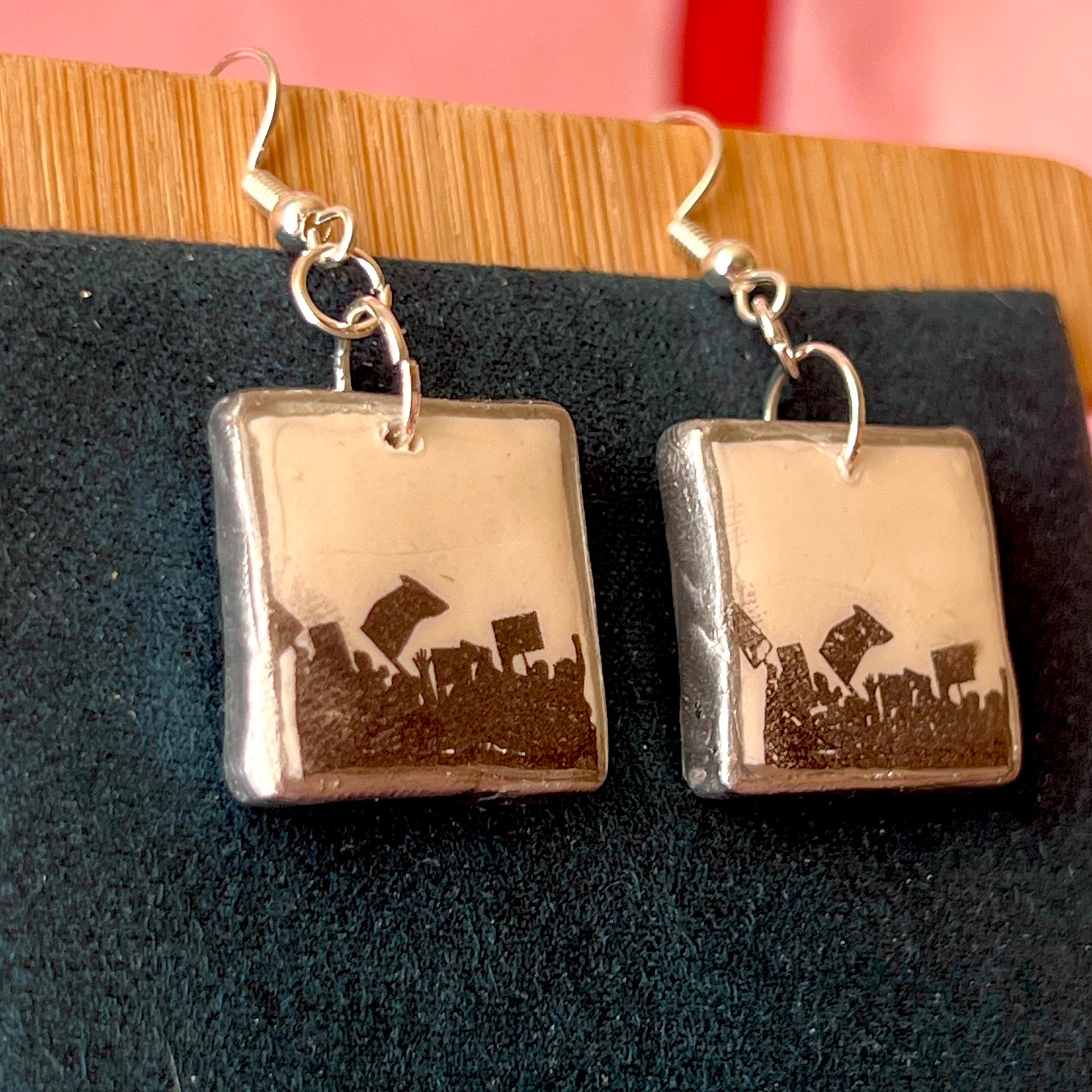Alt text: Activist “for the people” protest earrings featuring handmade polymer clay silhouette charms with a silver‑black metallic finish, silver‑plated hypoallergenic hooks, and bold protest jewelry style.