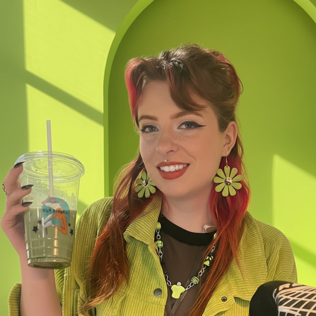 Woman with colorful hair holding a drink against a bright green wall.