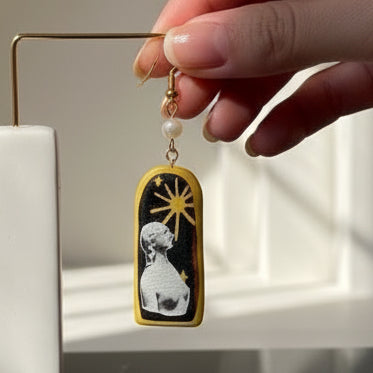 Pair of earrings with a design of a woman and sun, on a black background