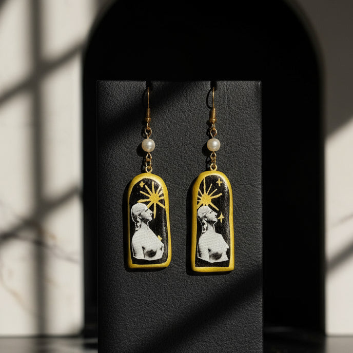Pair of earrings with a design of a woman and sun, on a dark background