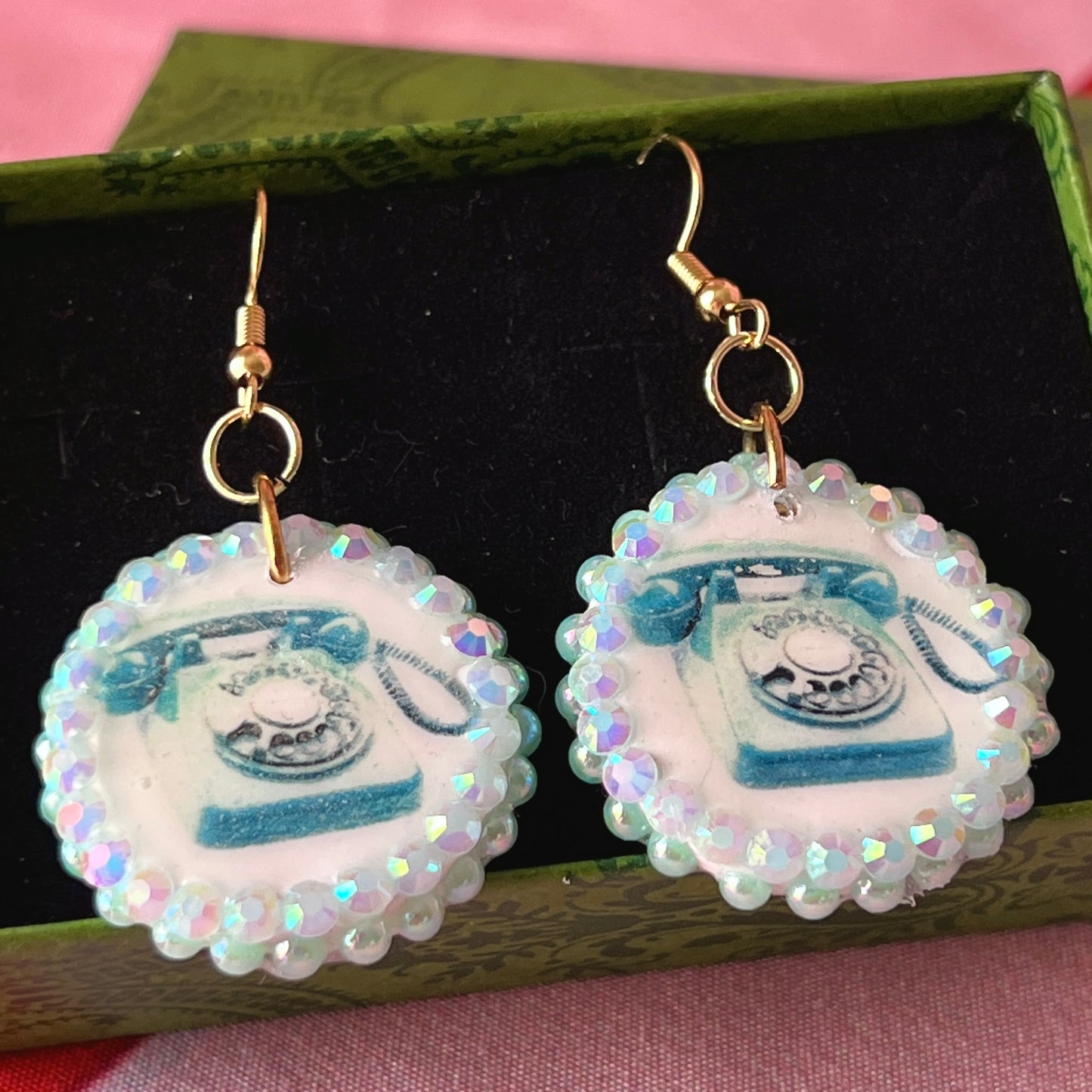 A handcrafted pair of iridescent teal dial‑up phone earrings made from polymer clay, featuring luminous pearl detailing, 18k gold‑plated hypoallergenic hooks, and a nostalgic Y2K, maximalist, statement‑jewelry vibe.