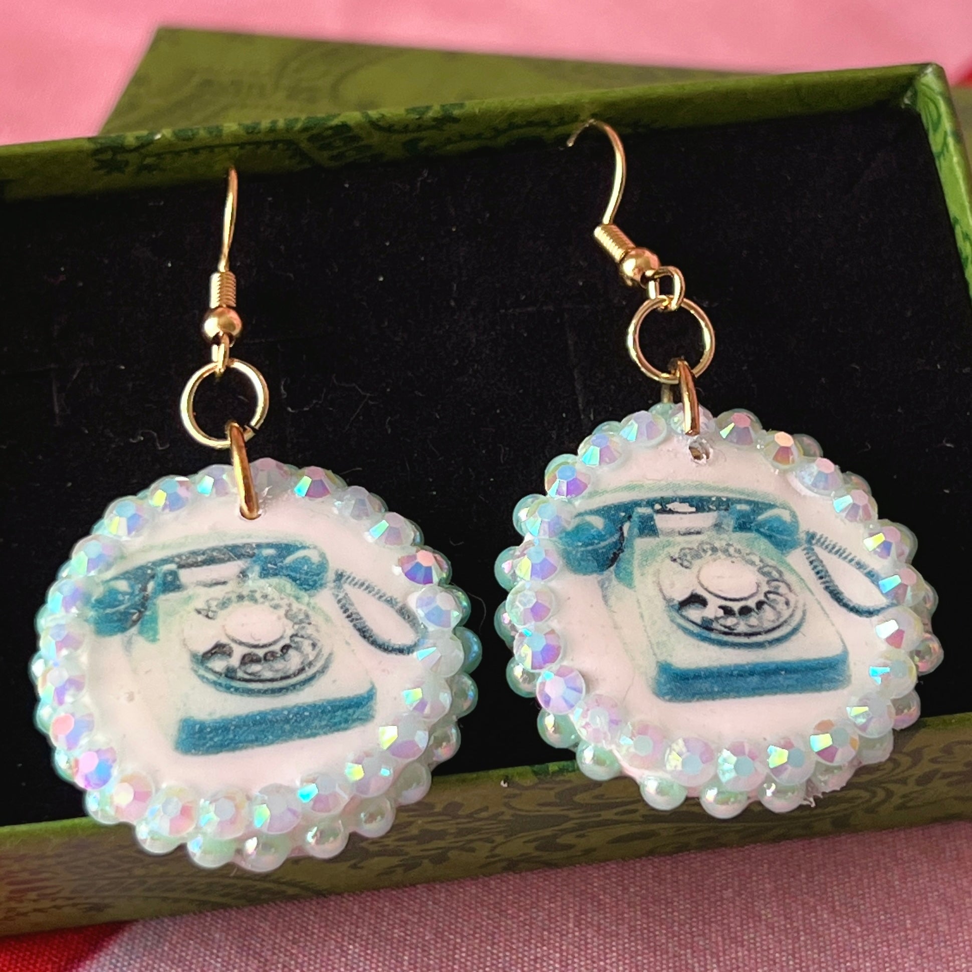 A handcrafted pair of iridescent teal dial‑up phone earrings made from polymer clay, featuring luminous pearl detailing, 18k gold‑plated hypoallergenic hooks, and a nostalgic Y2K, maximalist, statement‑jewelry vibe.