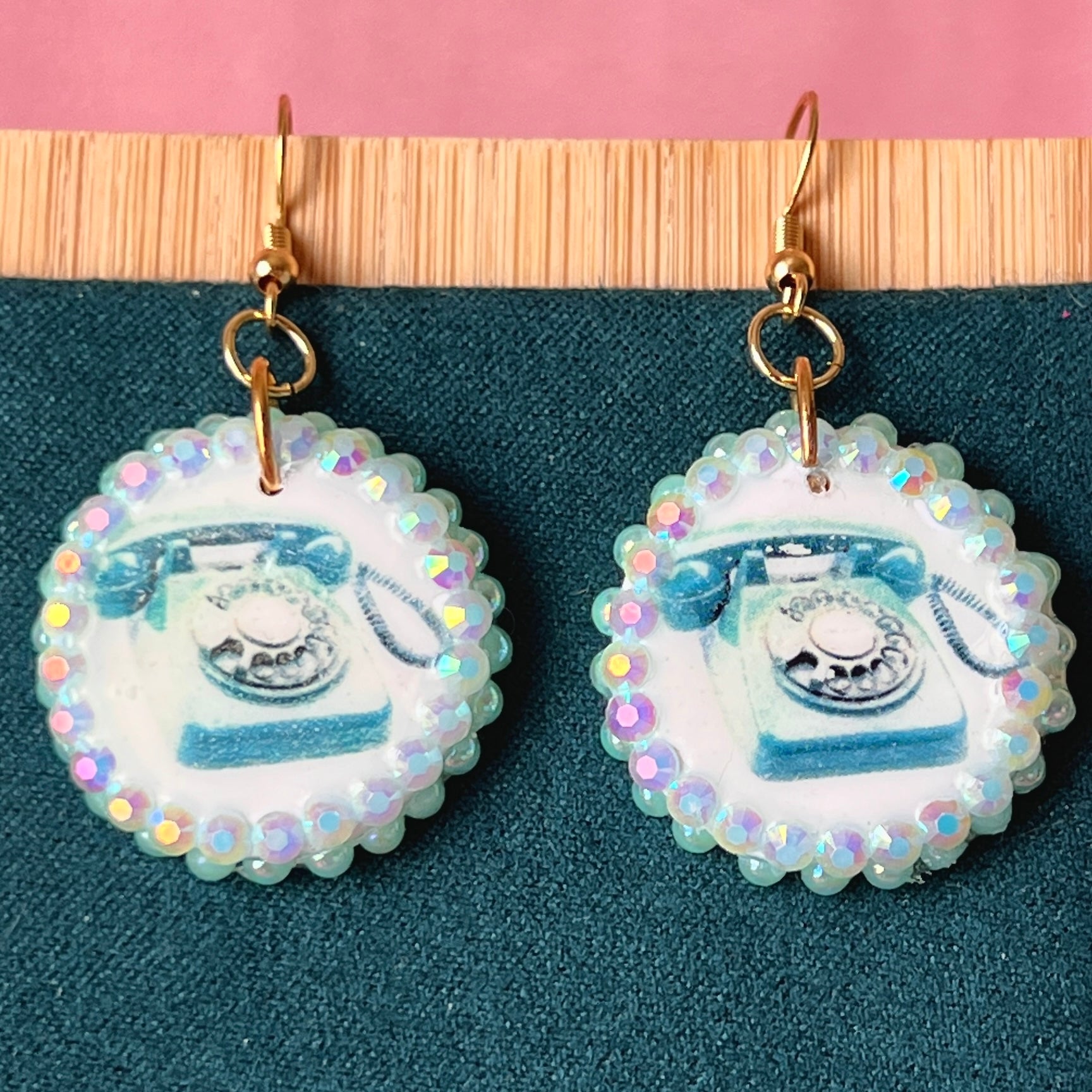 A handcrafted pair of iridescent teal dial‑up phone earrings made from polymer clay, featuring luminous pearl detailing, 18k gold‑plated hypoallergenic hooks, and a nostalgic Y2K, maximalist, statement‑jewelry vibe.