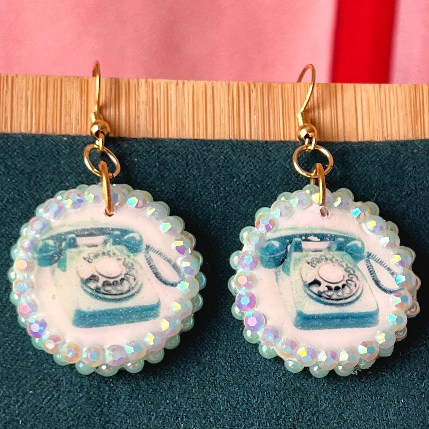 A handcrafted pair of iridescent teal dial‑up phone earrings made from polymer clay, featuring luminous pearl detailing, 18k gold‑plated hypoallergenic hooks, and a nostalgic Y2K, maximalist, statement‑jewelry vibe.
