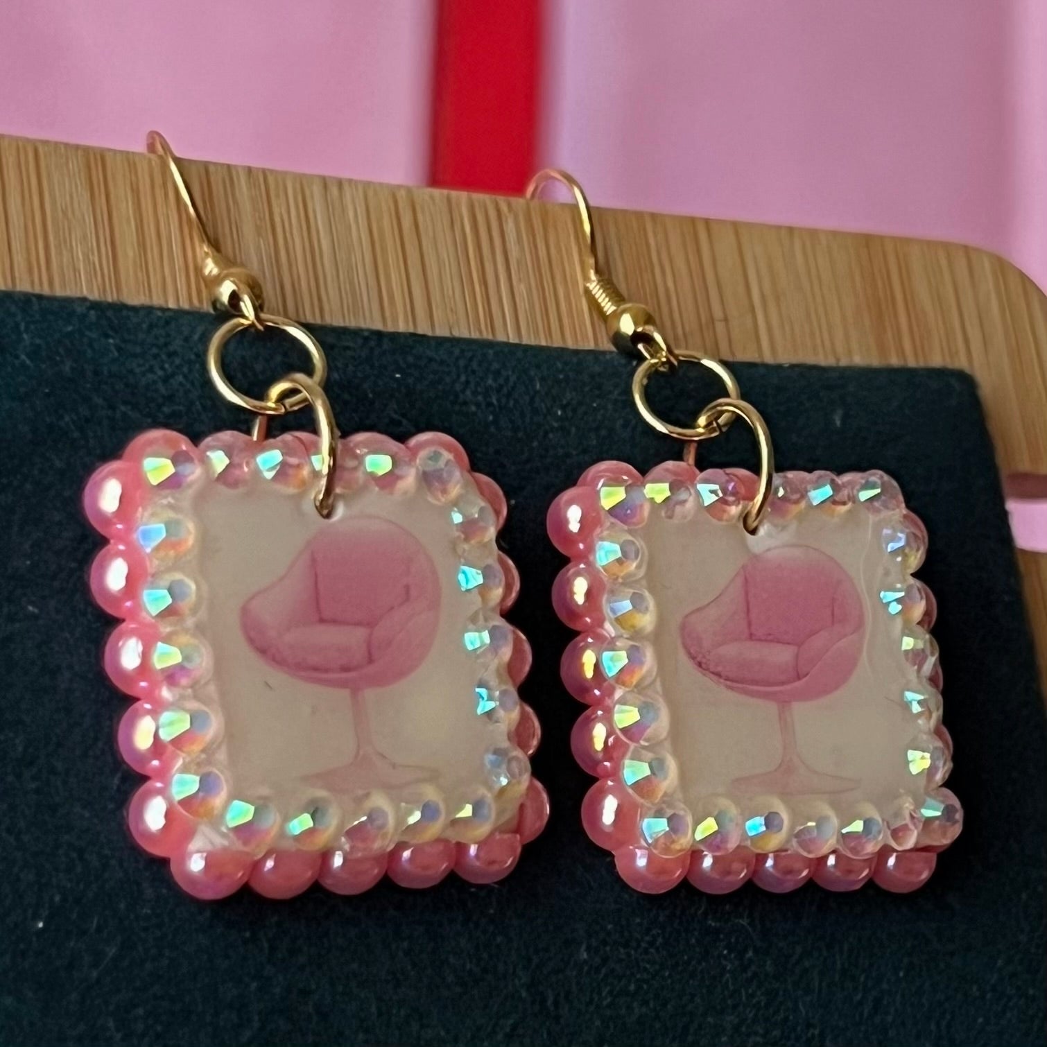 Handmade polymer‑clay earrings featuring a vintage mid‑century pink chair graphic framed by pink pearls and rhinestones on 18k gold‑plated hooks, perfect retro, vintage, indie, Y2K‑style statement dangles.