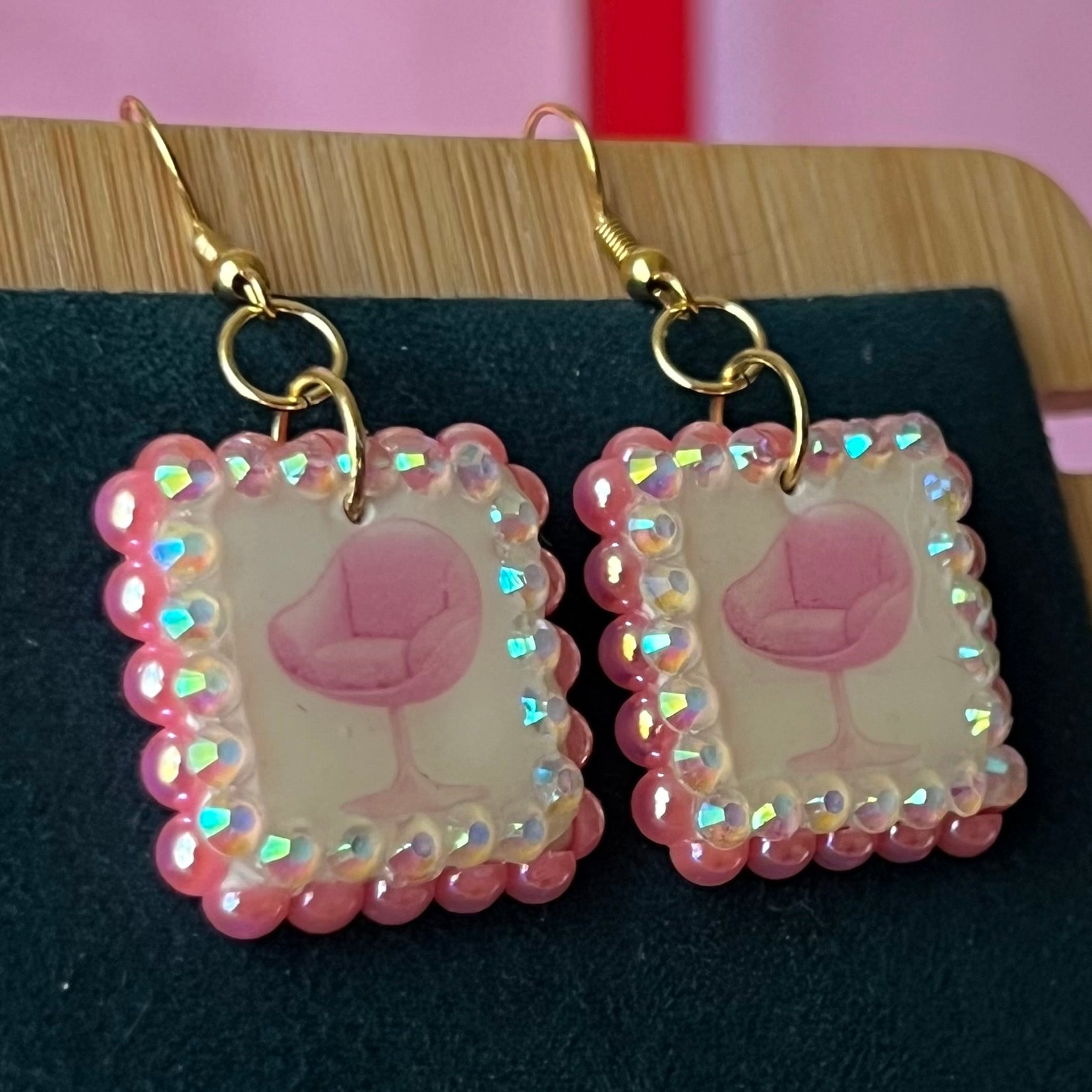 Handmade polymer‑clay earrings featuring a vintage mid‑century pink chair graphic framed by pink pearls and rhinestones on 18k gold‑plated hooks, perfect retro, vintage, indie, Y2K‑style statement dangles.