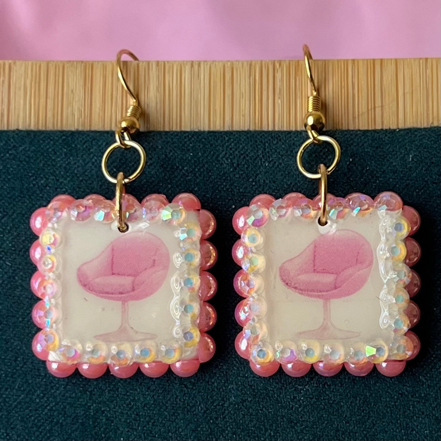 Handmade polymer‑clay earrings featuring a vintage mid‑century pink chair graphic framed by pink pearls and rhinestones on 18k gold‑plated hooks, perfect retro, vintage, indie, Y2K‑style statement dangles.
