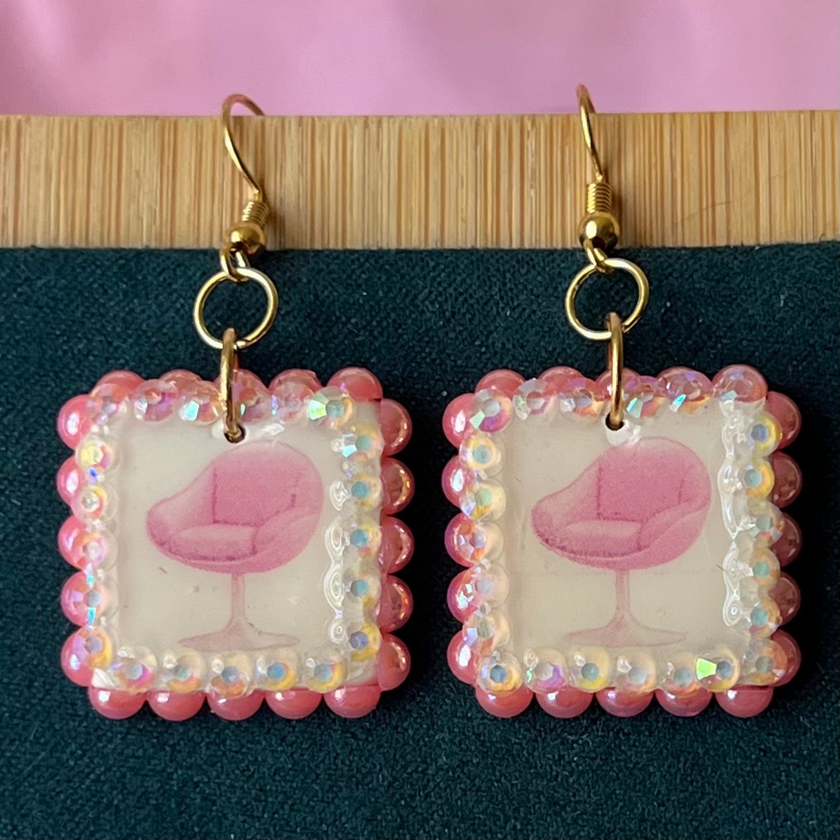 Handmade polymer‑clay earrings featuring a vintage mid‑century pink chair graphic framed by pink pearls and rhinestones on 18k gold‑plated hooks, perfect retro, vintage, indie, Y2K‑style statement dangles.