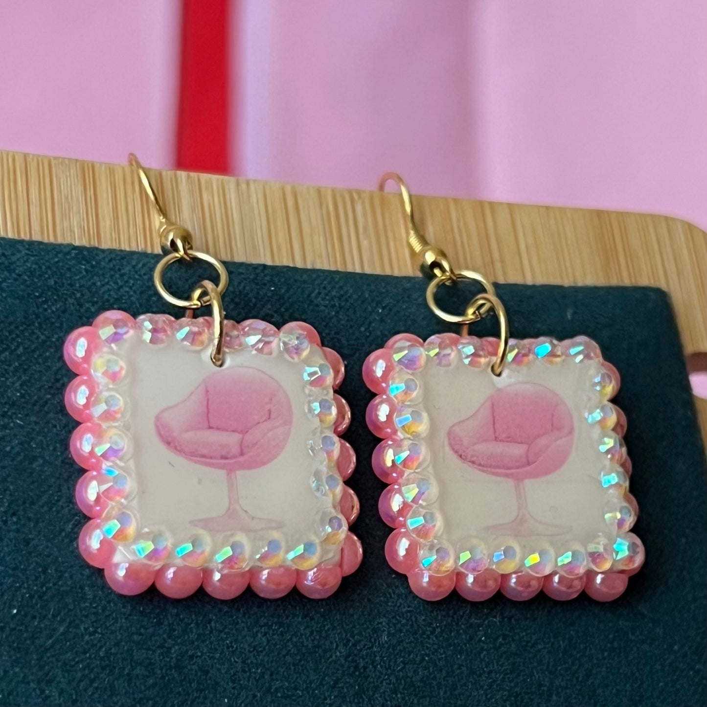 Handmade polymer‑clay earrings featuring a vintage mid‑century pink chair graphic framed by pink pearls and rhinestones on 18k gold‑plated hooks, perfect retro, vintage, indie, Y2K‑style statement dangles.