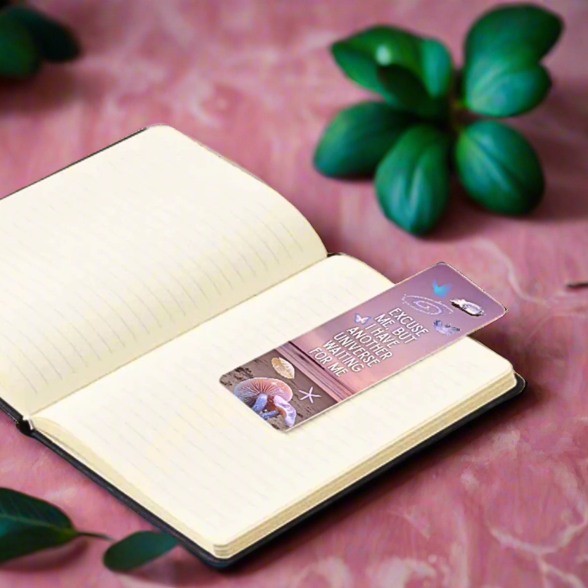 Pink ocean themed bookmark with text that reads "Excuse me, but I have another universe waiting for me" and illustration collage of shells on a pink background with green leaves