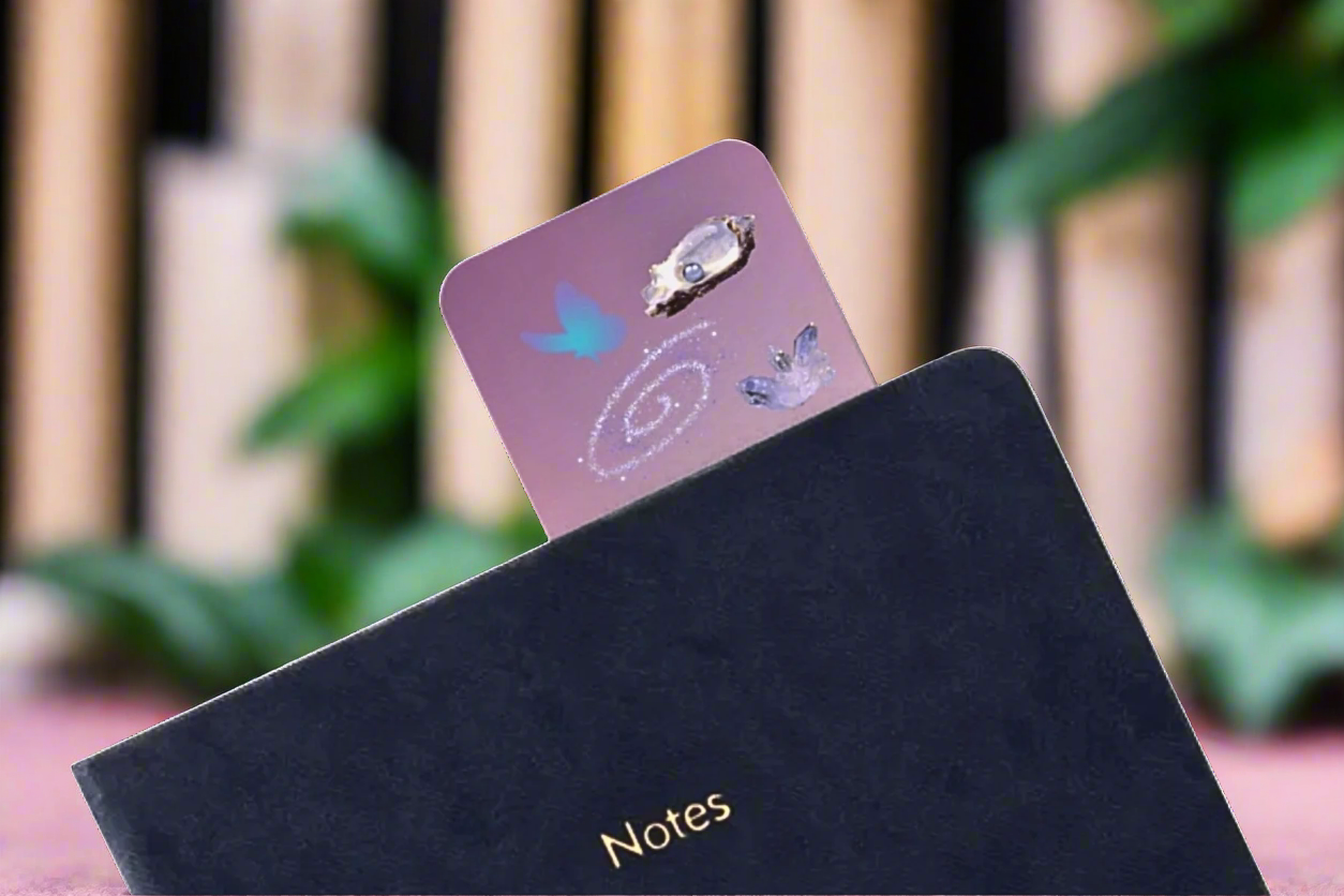 Black notebook with a pink and purple card bookmark ocean designs on a blurred background