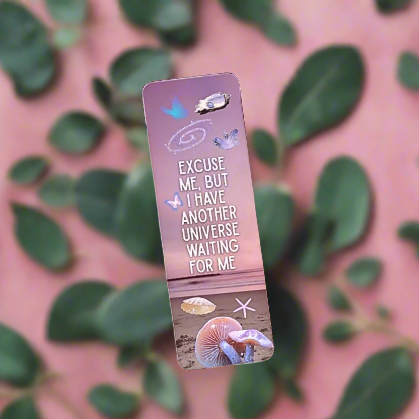 Pink ocean themed bookmark with text that reads "Excuse me, but I have another universe waiting for me" and illustration collage of shells on a pink background with green leaves