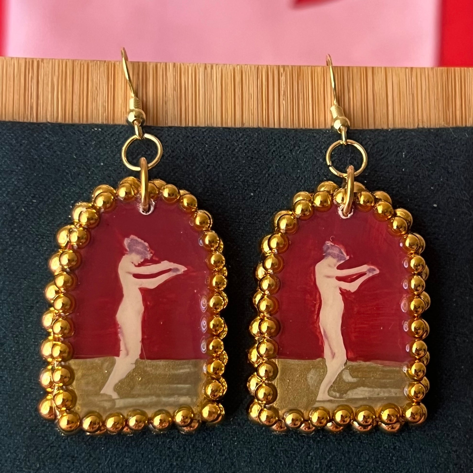 Handmade polymer‑clay arch‑shaped earrings featuring a nude lady art portrait on a deep red background, framed with pearls and finished with 18k gold‑plated hypoallergenic hooks—perfect romantic, coquette, renaissance‑style statement piece.