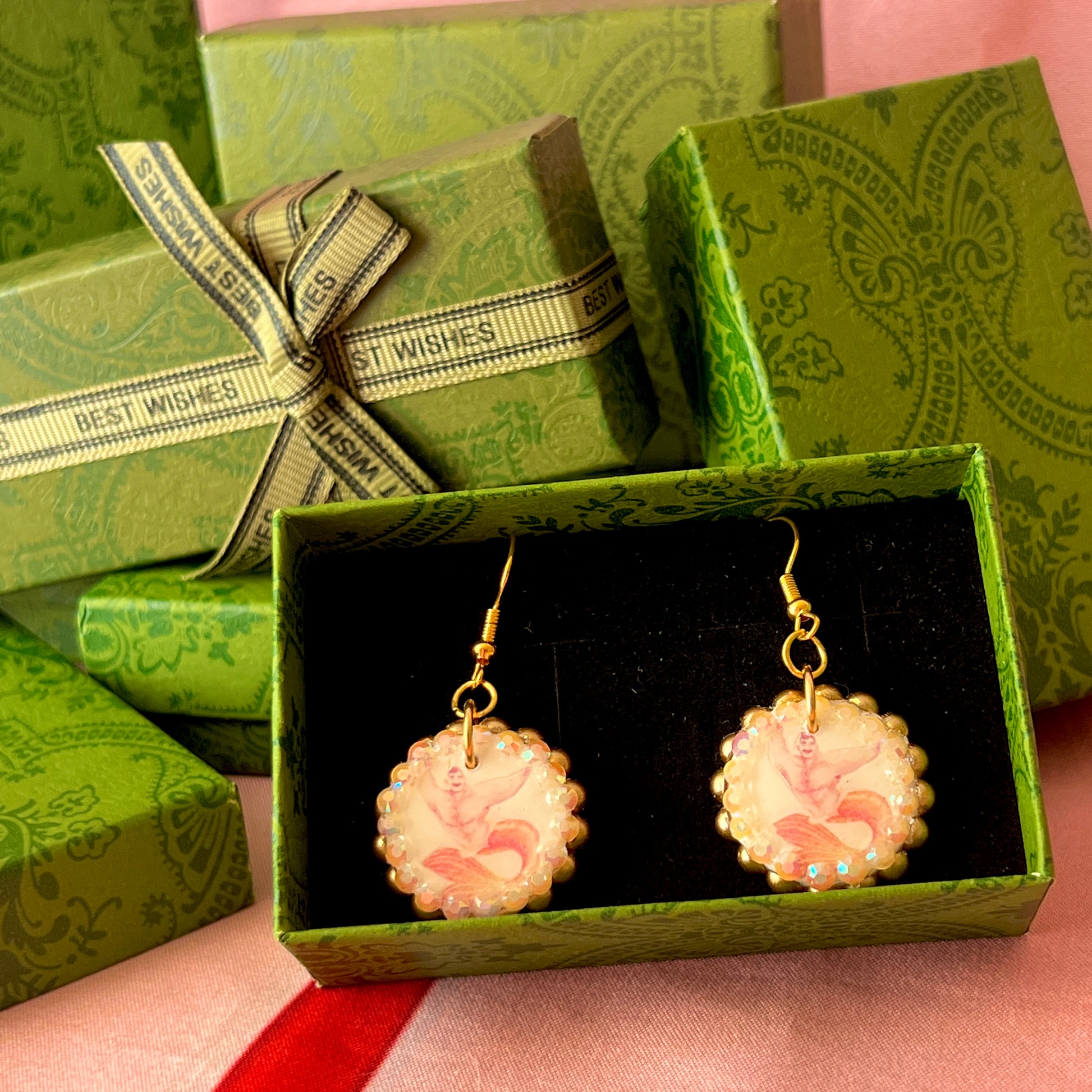 Handmade mermaid‑core earrings featuring a polymer‑clay merman portrait, 3D bow, orange pearls, rhinestones, and 18k gold‑plated hypoallergenic findings—whimsical, nostalgic, wearable art perfect for a statement look.