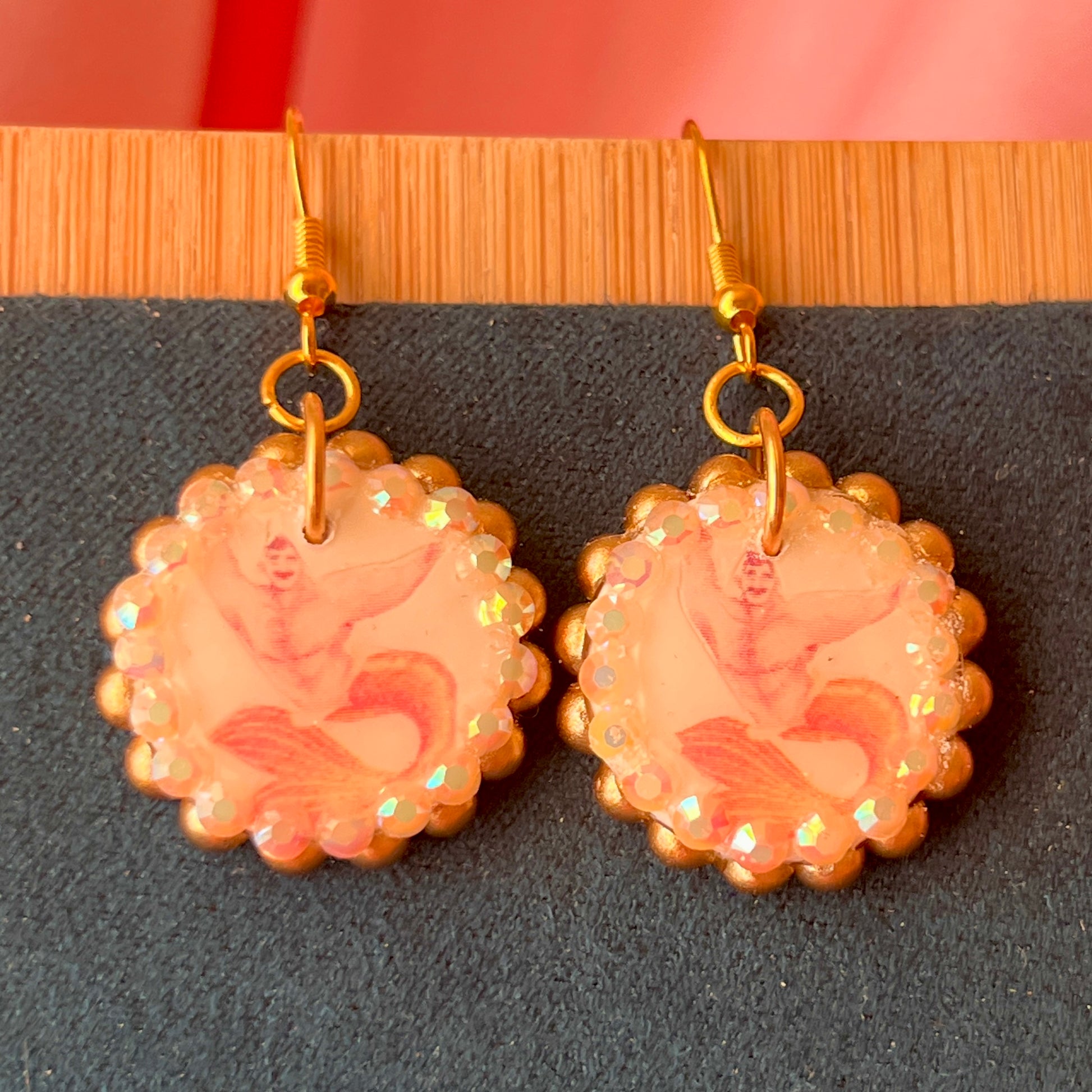 Handmade mermaid‑core earrings featuring a polymer‑clay merman portrait, 3D bow, orange pearls, rhinestones, and 18k gold‑plated hypoallergenic findings—whimsical, nostalgic, wearable art perfect for a statement look.