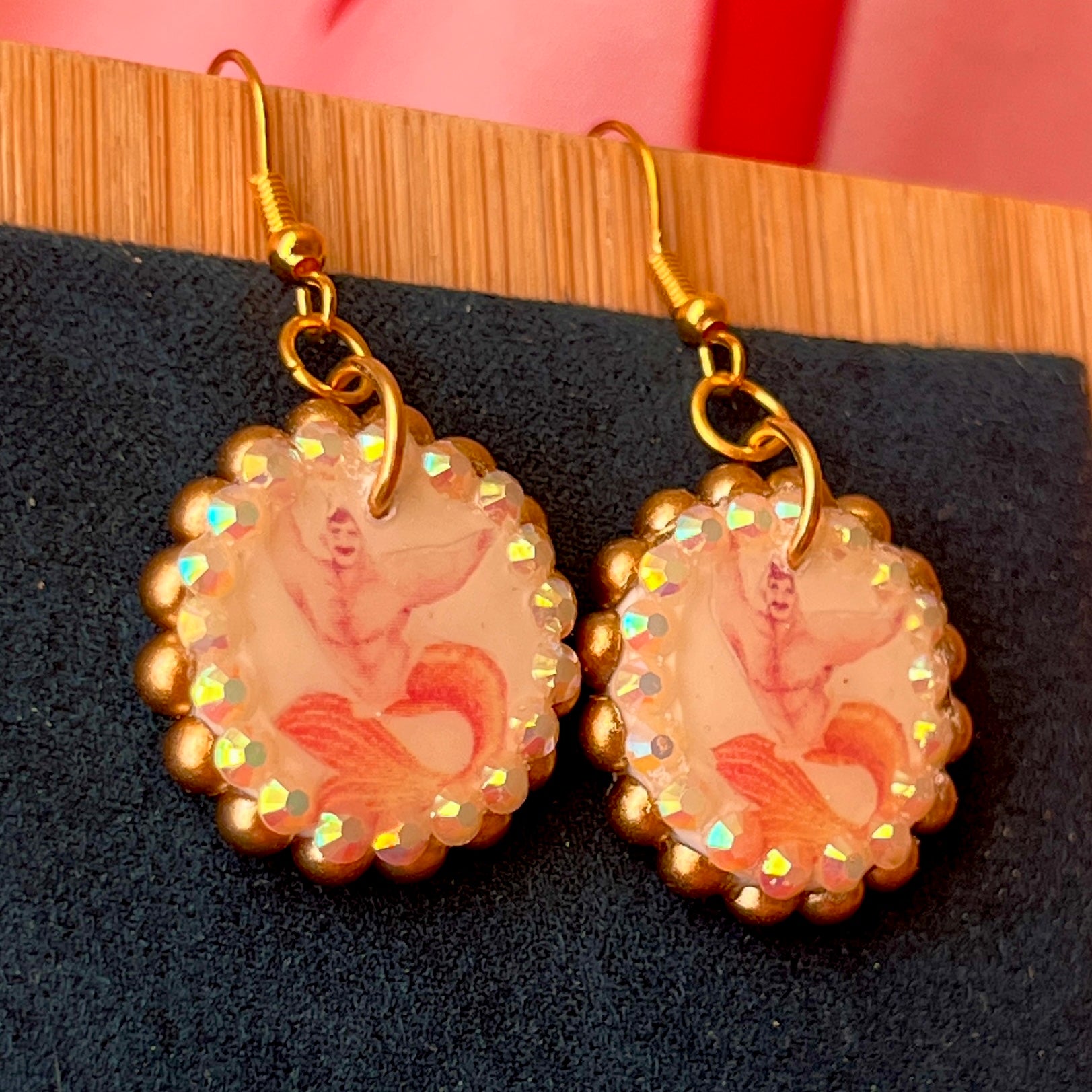 Handmade mermaid‑core earrings featuring a polymer‑clay merman portrait, 3D bow, orange pearls, rhinestones, and 18k gold‑plated hypoallergenic findings—whimsical, nostalgic, wearable art perfect for a statement look.
