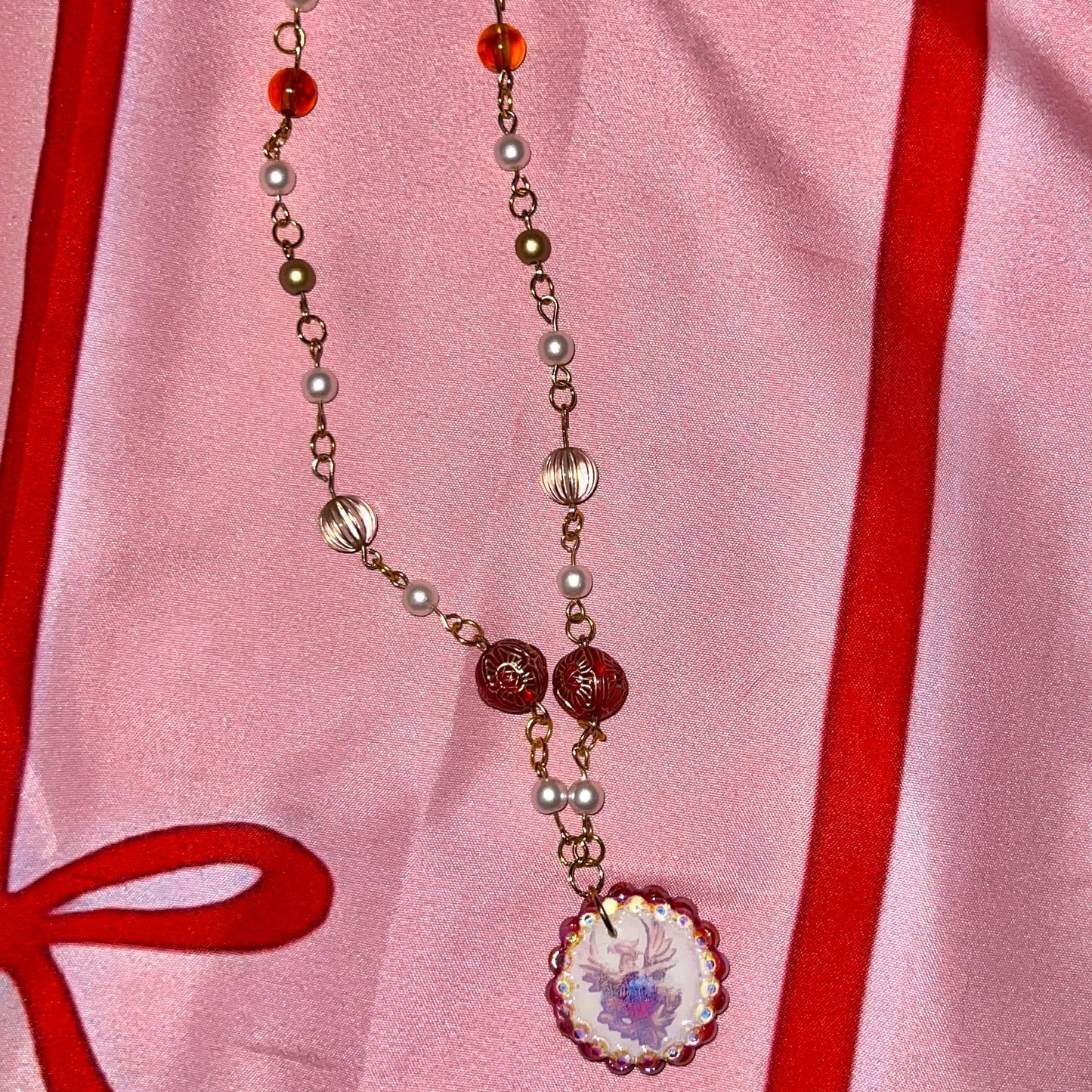Alt text: A regal, medieval‑inspired pair of earrings featuring a golden phoenix sigil cradling a crimson gem, bedazzled with deep red and iridescent pearl‑like beads, perfect for fantasy, renaissance fair, and royal‑style looks.