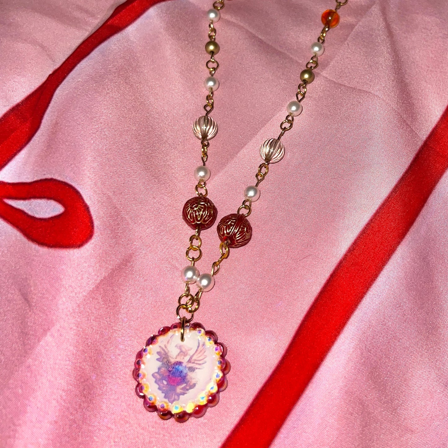 Alt text: A regal, medieval‑inspired pair of earrings featuring a golden phoenix sigil cradling a crimson gem, bedazzled with deep red and iridescent pearl‑like beads, perfect for fantasy, renaissance fair, and royal‑style looks.
