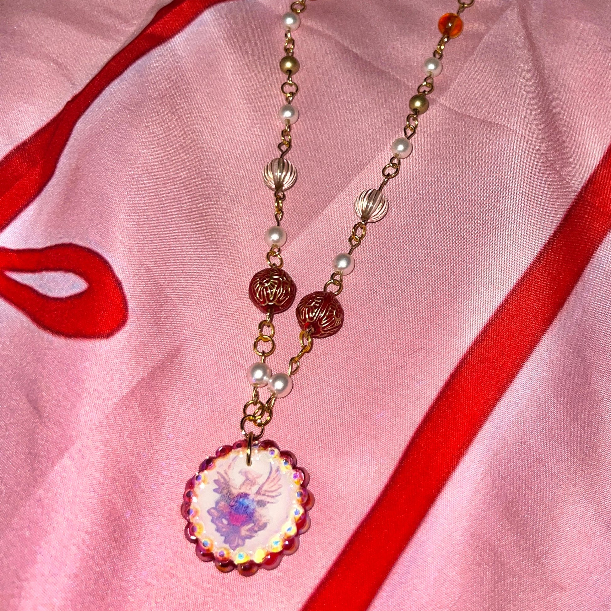 Alt text: A regal, medieval‑inspired pair of earrings featuring a golden phoenix sigil cradling a crimson gem, bedazzled with deep red and iridescent pearl‑like beads, perfect for fantasy, renaissance fair, and royal‑style looks.