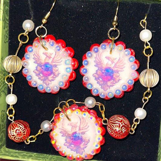 Alt text: A regal, medieval‑inspired pair of earrings featuring a golden phoenix sigil cradling a crimson gem, bedazzled with deep red and iridescent pearl‑like beads, perfect for fantasy, renaissance fair, and royal‑style looks.