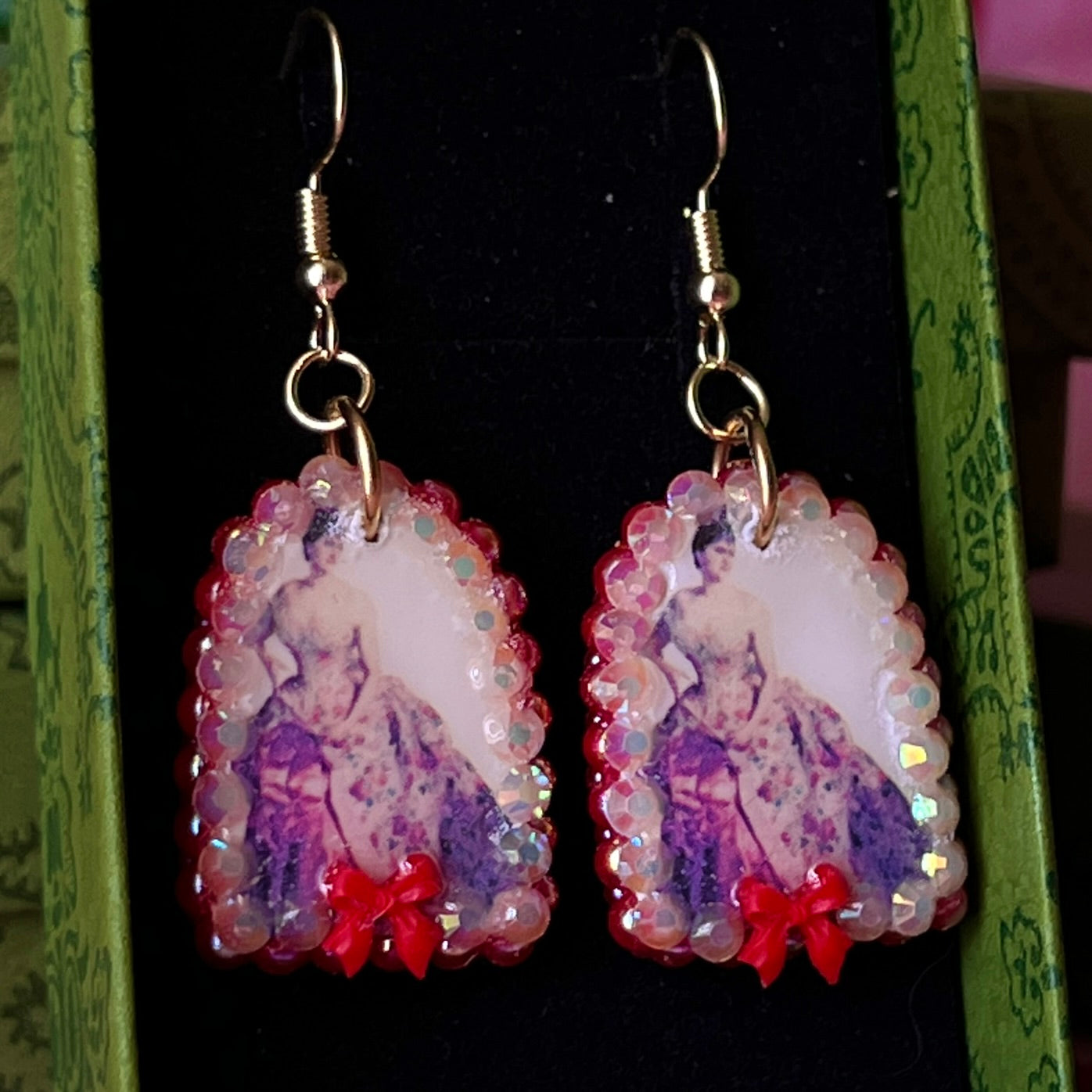 Alt text: A wearable art earring inspired by a Victorian romance portrait, featuring a polymer‑clay art print charm embellished with iridescent pearls, clear rhinestones, and a red coquette bow, hanging from gold‑plated hooks—perfect for museum‑core, renaissance‑core, and art‑lover styling.