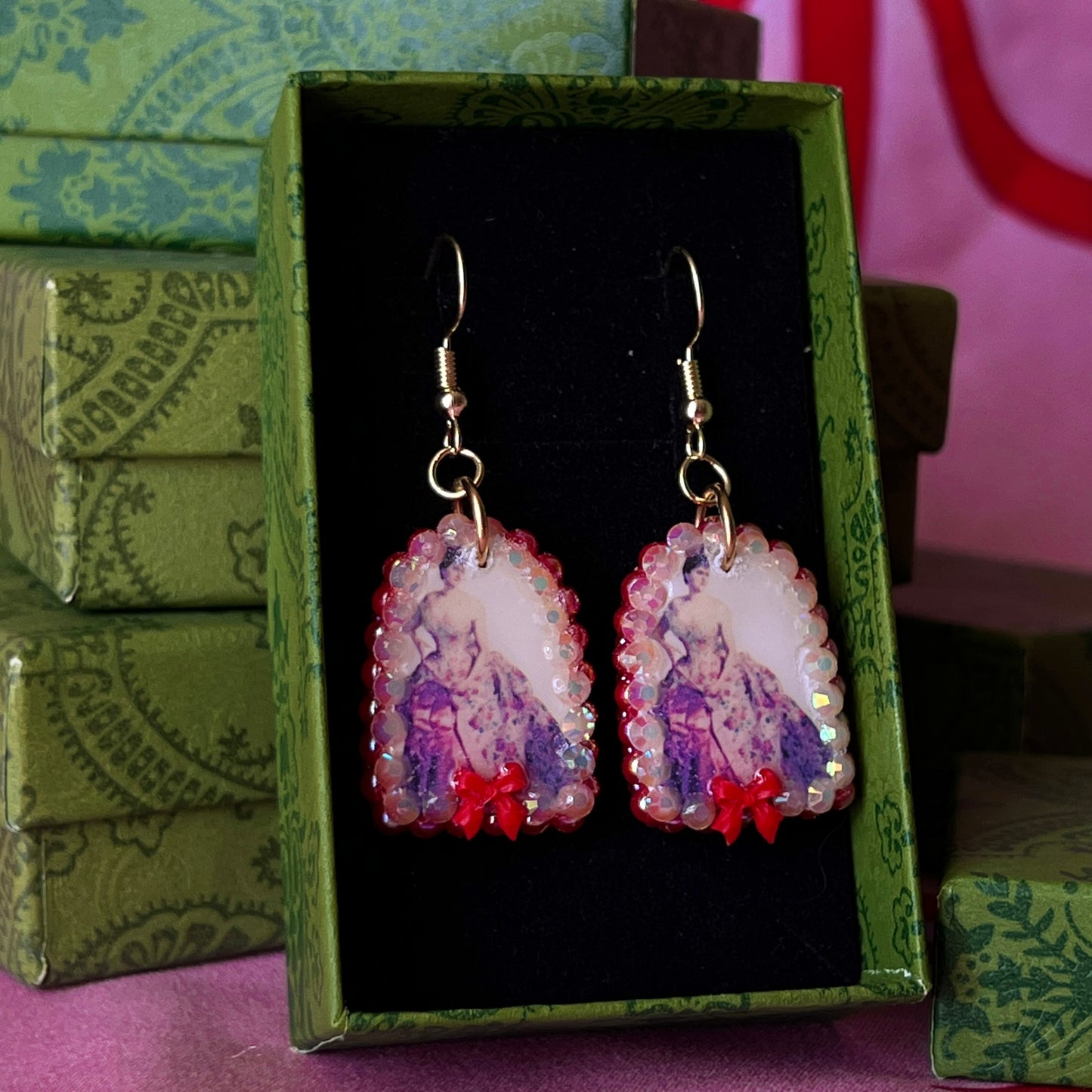 Alt text: A wearable art earring inspired by a Victorian romance portrait, featuring a polymer‑clay art print charm embellished with iridescent pearls, clear rhinestones, and a red coquette bow, hanging from gold‑plated hooks—perfect for museum‑core, renaissance‑core, and art‑lover styling.