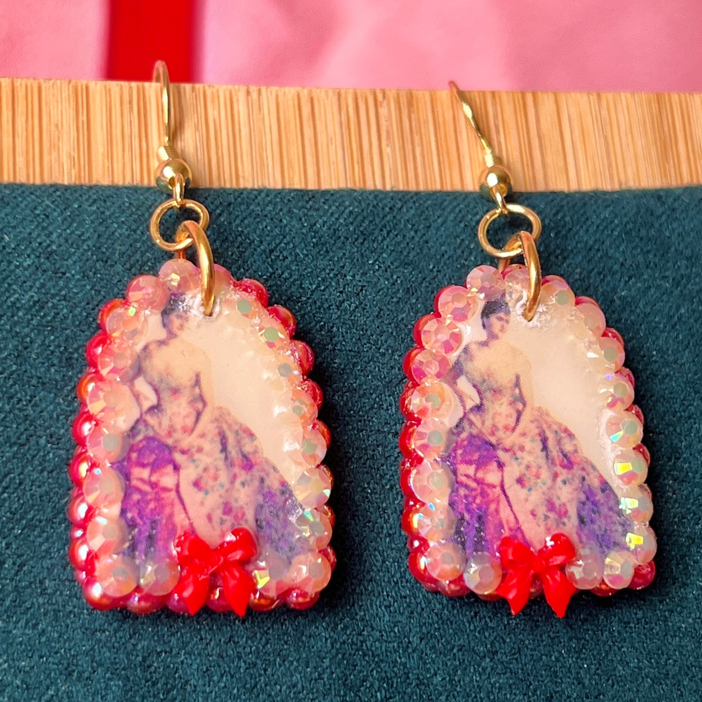 Alt text: A wearable art earring inspired by a Victorian romance portrait, featuring a polymer‑clay art print charm embellished with iridescent pearls, clear rhinestones, and a red coquette bow, hanging from gold‑plated hooks—perfect for museum‑core, renaissance‑core, and art‑lover styling.