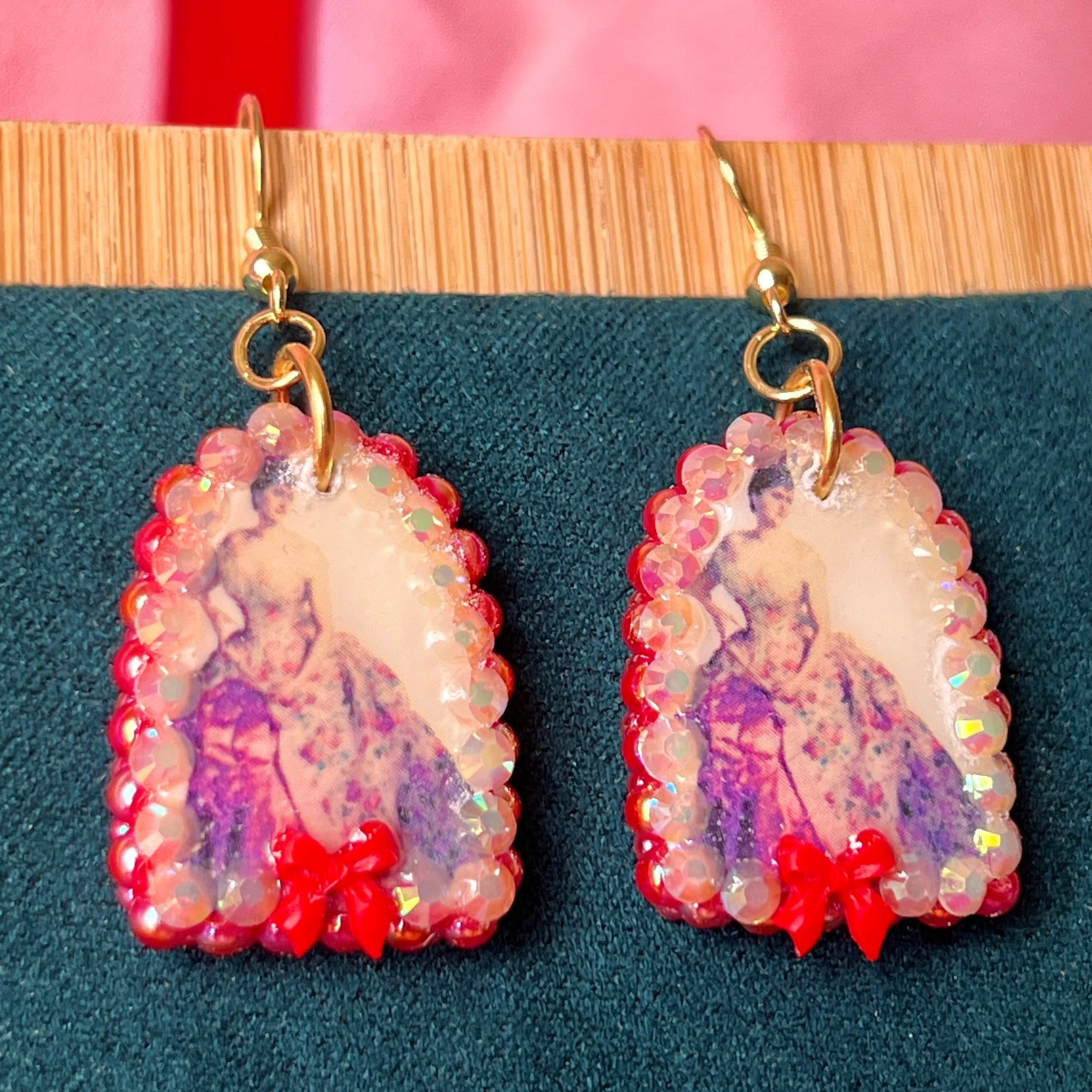 Alt text: A wearable art earring inspired by a Victorian romance portrait, featuring a polymer‑clay art print charm embellished with iridescent pearls, clear rhinestones, and a red coquette bow, hanging from gold‑plated hooks—perfect for museum‑core, renaissance‑core, and art‑lover styling.