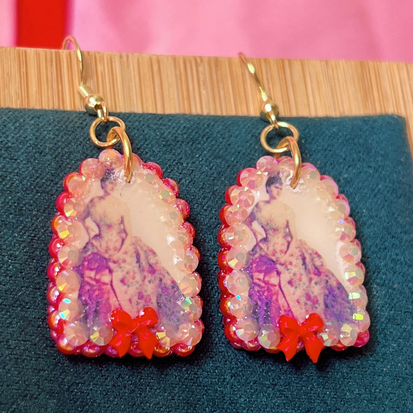 Alt text: A wearable art earring inspired by a Victorian romance portrait, featuring a polymer‑clay art print charm embellished with iridescent pearls, clear rhinestones, and a red coquette bow, hanging from gold‑plated hooks—perfect for museum‑core, renaissance‑core, and art‑lover styling.