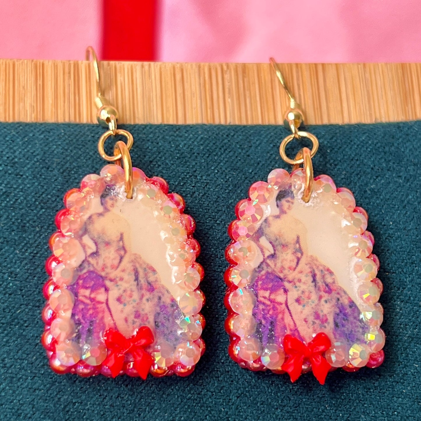 Alt text: A wearable art earring inspired by a Victorian romance portrait, featuring a polymer‑clay art print charm embellished with iridescent pearls, clear rhinestones, and a red coquette bow, hanging from gold‑plated hooks—perfect for museum‑core, renaissance‑core, and art‑lover styling.