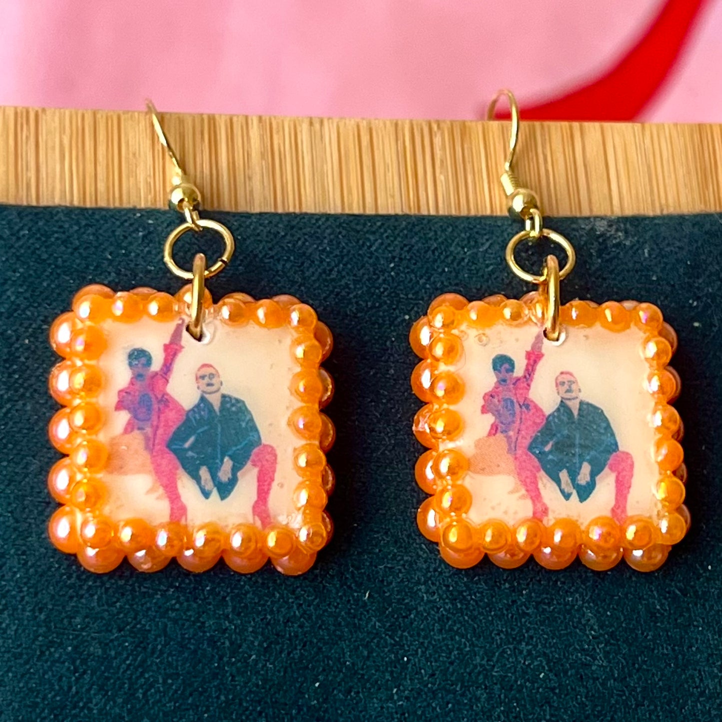 Handmade queer art earrings featuring polymer‑clay square charms with a “Strike a Pose” design, iridescent orange pearl drops, and 18k gold‑plated hypoallergenic findings – lightweight square charms, LGBTQ‑pride, statement piece, ready to ship in 1–3 days.